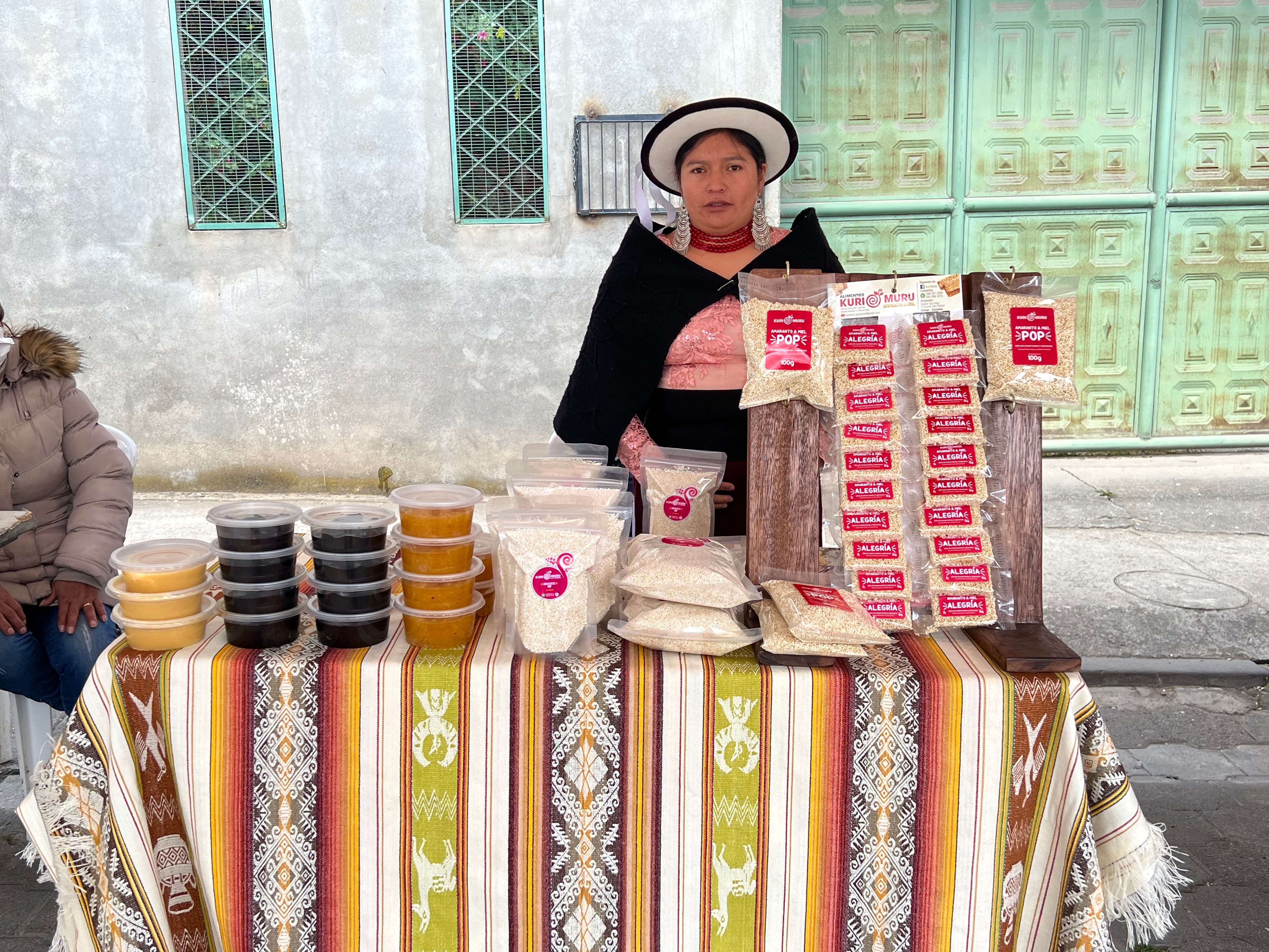 A well-dressed Cañari woman selling various grains from a table on the street